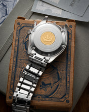 Load image into Gallery viewer, Silver watch with a gold emblem on a textured surface