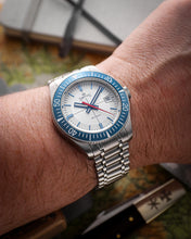 Load image into Gallery viewer, Silver watch with blue bezel on a wrist, blurred background