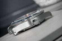 Load image into Gallery viewer, Close-up of a silver watch with a dark bezel on a wooden surface
